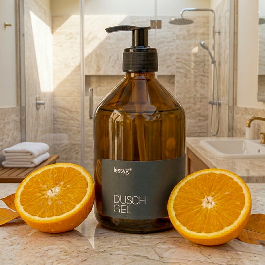 Braune Glas-Pumpflasche mit schwarzem Etikett „Duschgel“ steht auf einem hellen untergrund in einer modernen Dusche mit beigen Fliesen; daneben liegen halbierte Orangen